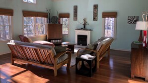 A spacious living room with a fireplace, wooden furniture, and large windows. - Lake Michigan Home on Tunnel of Trees with Game Room and Views (Harbor Springs)