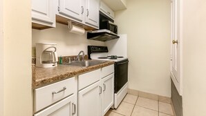 A compact kitchen with white cabinets, a built-in microwave, a coffee maker, and a stove.