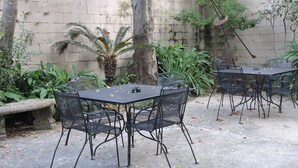A patio area with a table and chairs, surrounded by plants and a stone wall.
