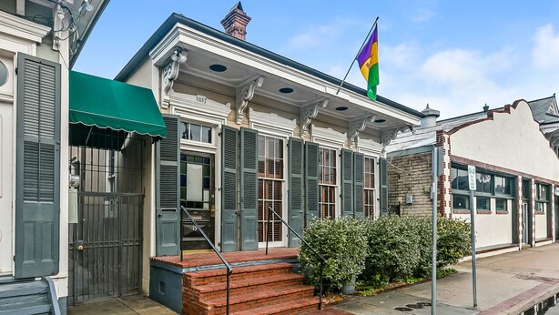 A historic building with a green awning, a flag, and a brick staircase leading to the entrance.
