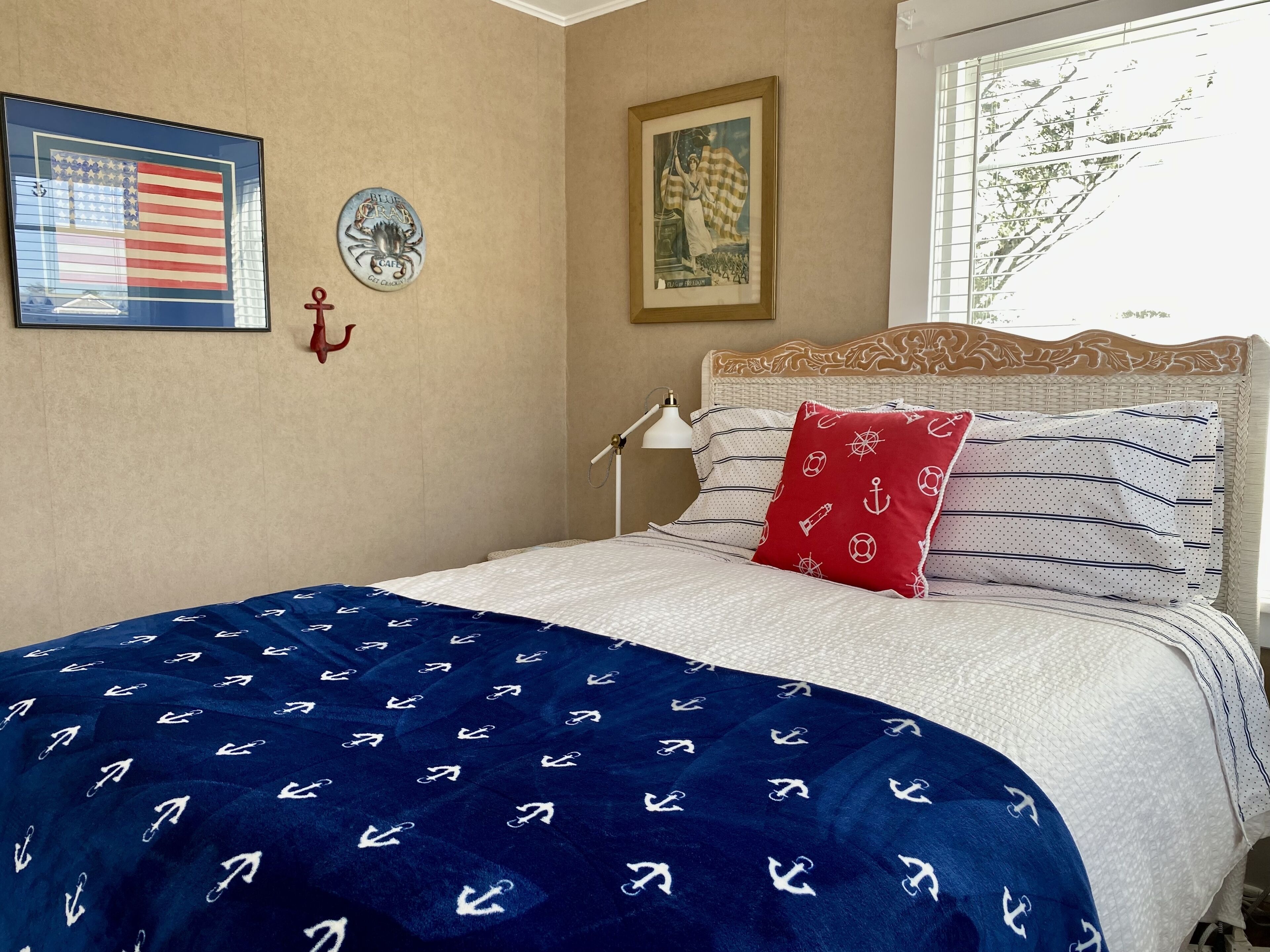 A bedroom with a bed, a nightstand, a lamp, a framed picture of a woman, and a wall with a framed American flag and a framed picture of a crab.