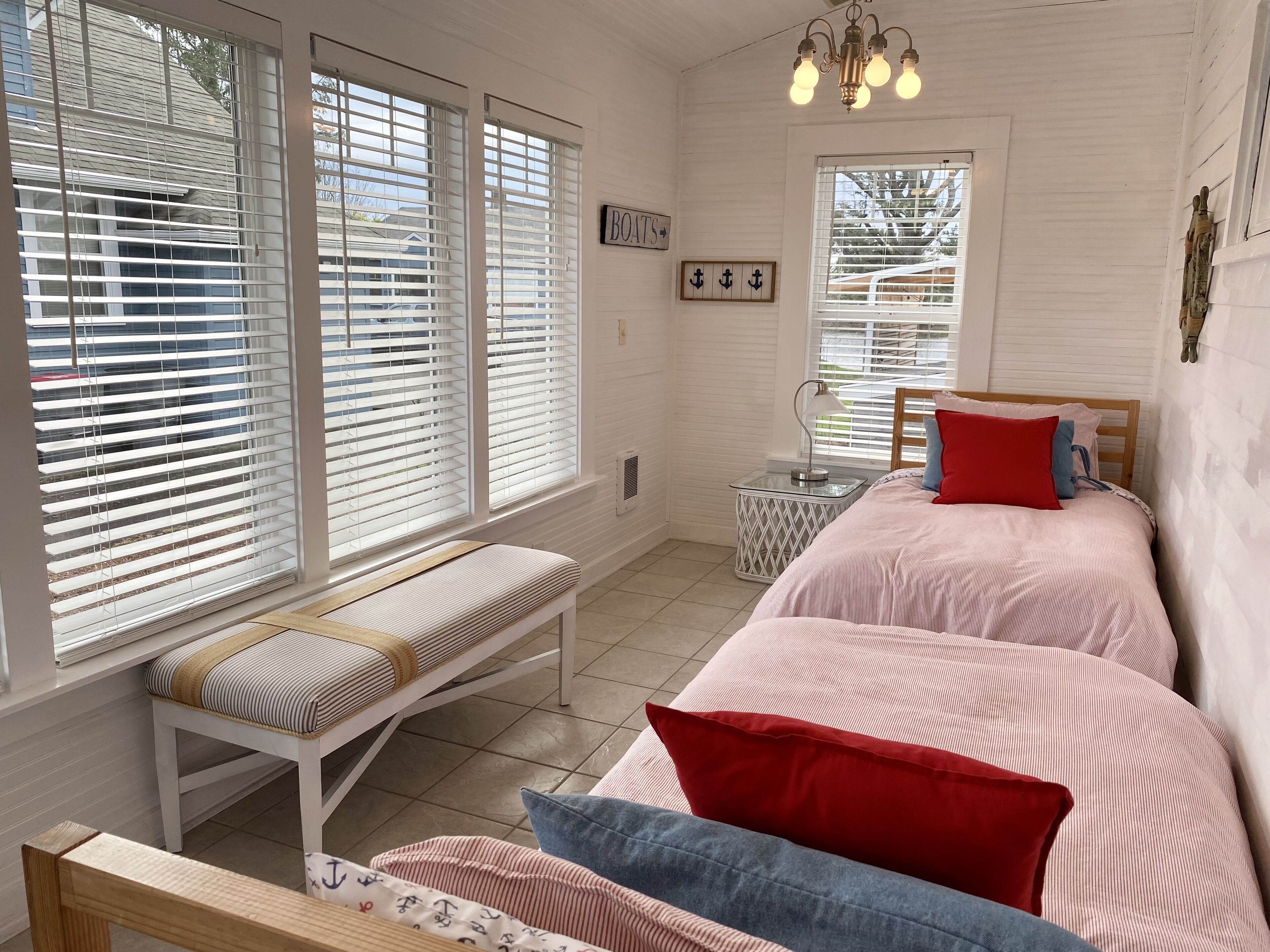 Une chambre à coucher comprenant un lit, un banc, une table de chevet et une fenêtre avec des stores.