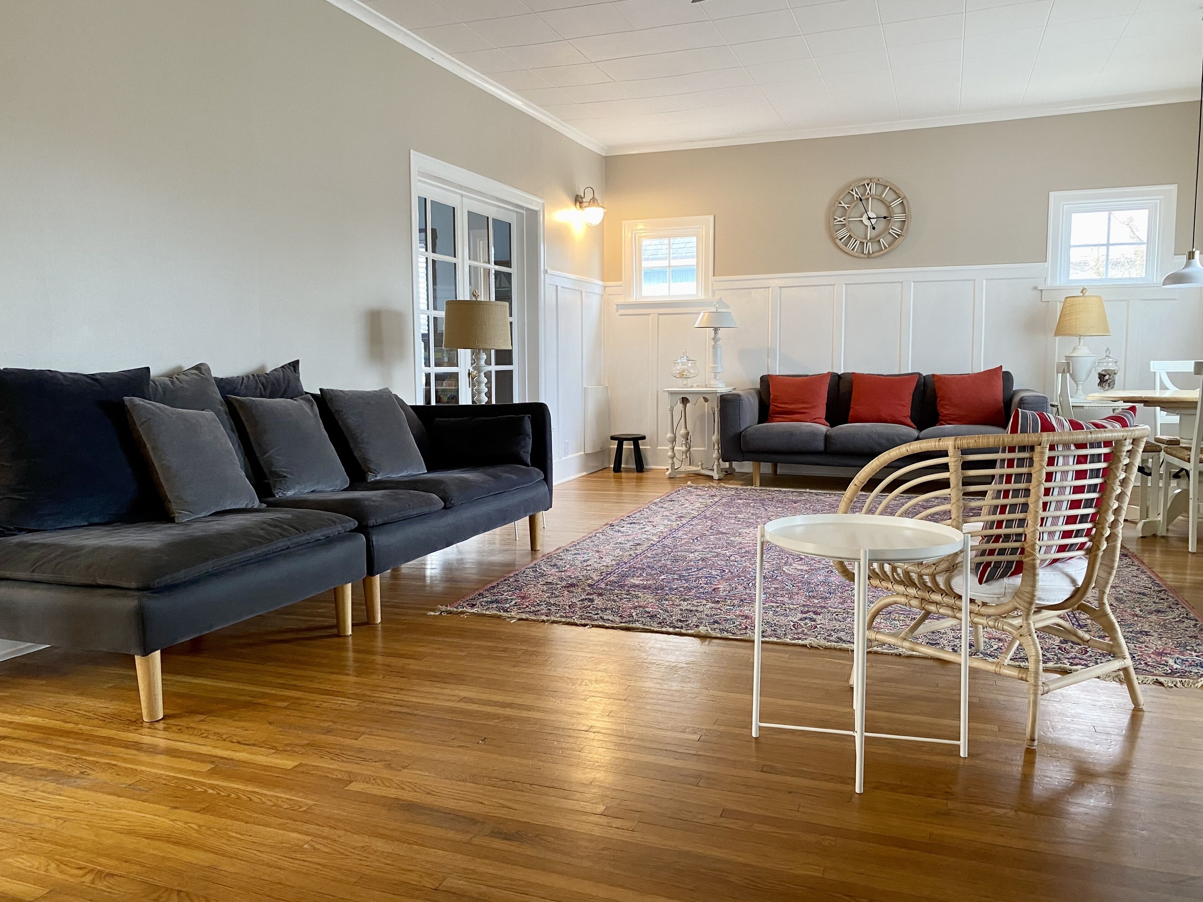 A living room with a dark grey sectional sofa, a round white table, and a wicker chair.
