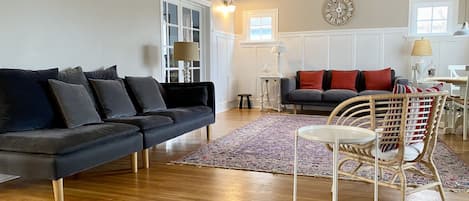A living room with a dark grey sectional sofa, a round white table, and a wicker chair.