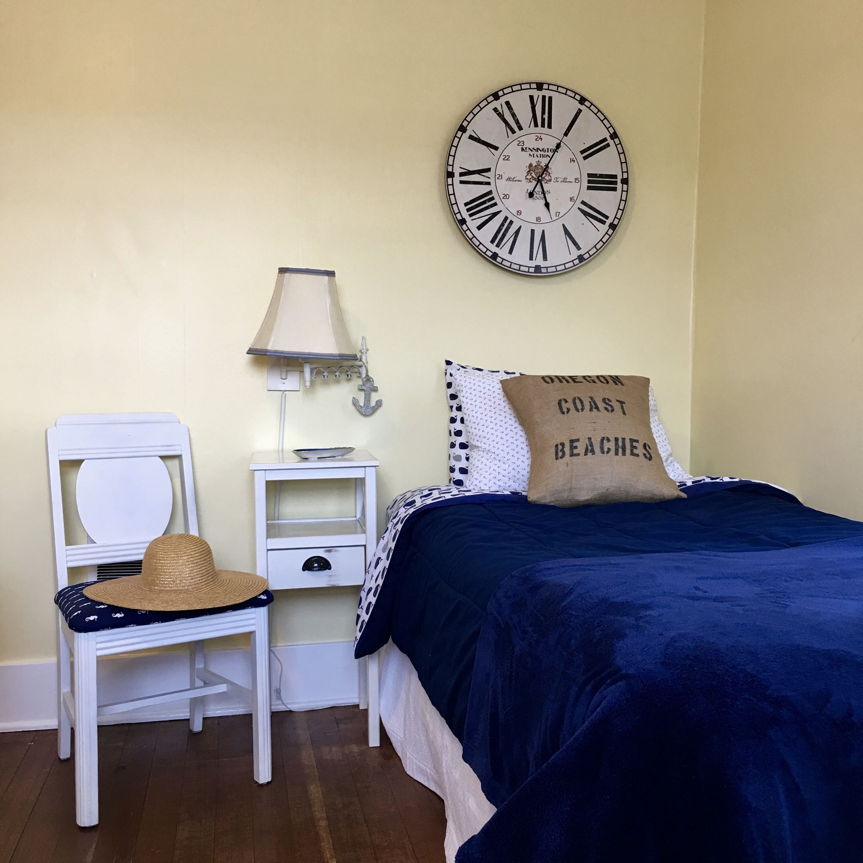 A bedroom with a bed, a nightstand, a lamp, a chair, and a wall clock.