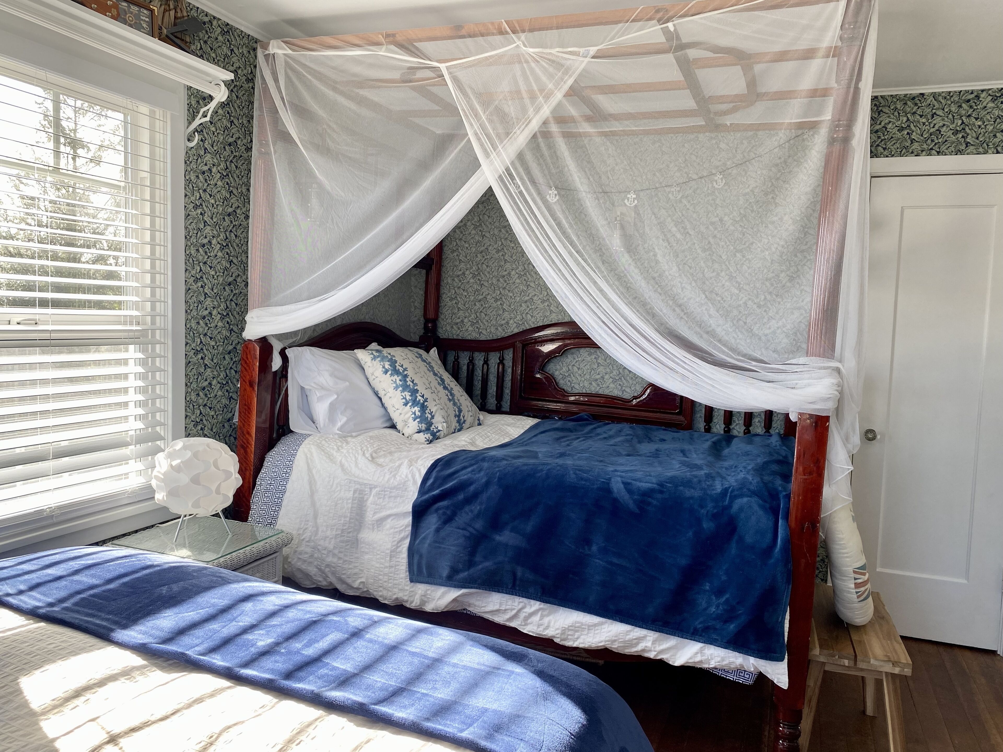 A bedroom with a canopy bed, a bench, and a window with blinds.