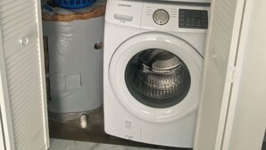 A laundry room with two stacked washing machines, a blue laundry basket, and a mop.