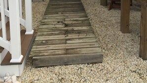 A narrow wooden pathway leading to a building with a white railing and a wooden deck.