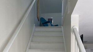 A white staircase with a handrail, leading to a landing where a blue chair is placed.