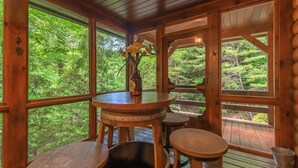 A wooden cabin interior with large windows, a round table with stools, and a vase with flowers. - Babbling Brook - 10 Minutes from Downtown Blue Ridge (Blue Ridge)