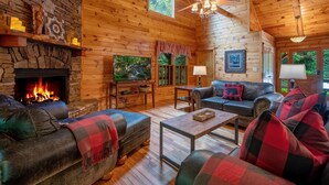 A cozy cabin interior with a stone fireplace, wooden walls, a ceiling fan, and a comfortable seating area. - Babbling Brook - 10 Minutes from Downtown Blue Ridge (Blue Ridge)