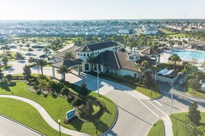 An aerial view of a residential area with a large house featuring a curved roof, a swimming pool, and a well-maintained lawn.