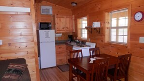 A cozy cabin-style kitchen with wooden walls, a dining table with chairs, a refrigerator, a microwave, and a stove.