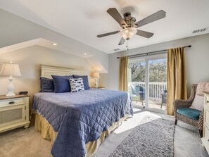 Un dormitorio con cama, mesitas de noche, ventilador de techo, ventana con cortinas y vistas al exterior.