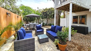 Eine Terrasse mit Korbmöbeln, einem Tisch und Stühlen, umgeben von einem Holzzaun und Blumentöpfen.