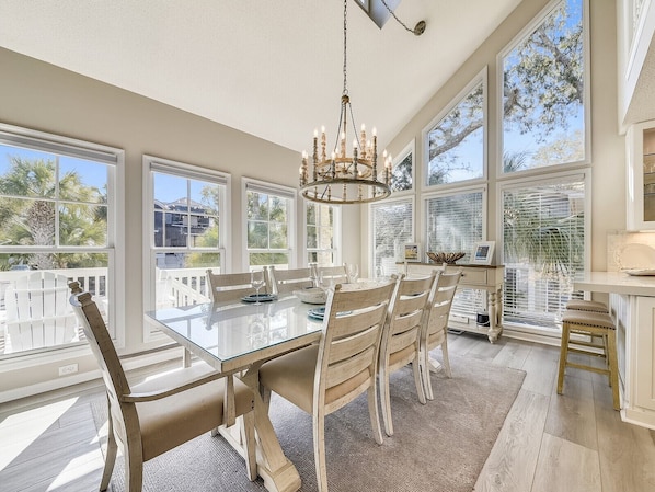A spacious dining area with a glass table and wooden chairs, large windows with a view, and a chandelier.