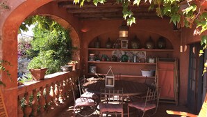 Eine Terrasse im Freien mit einem Holztisch und -stühlen, umgeben von Terrakottawänden und Blumentöpfen.