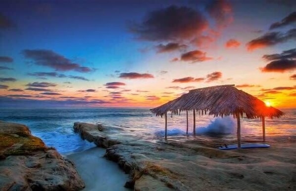 A beach with a thatched structure, rocky shoreline, and ocean waves.