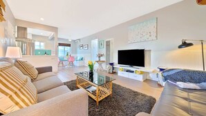 Una sala moderna con sofá, mesa de centro, televisor y un comedor al fondo.
