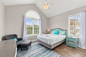 Quarto com cama, uma cadeira, mesa de cabeceira, luminária e ventilador de teto.