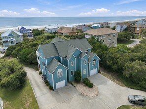 A multi-story residential building with a garage, surrounded by greenery and a view of the beach. - 2nd Row Duplex with elevator, views, community pool, and direct beach access. (Emerald Isle)