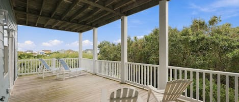 A covered outdoor deck with white railings and two Adirondack chairs.
