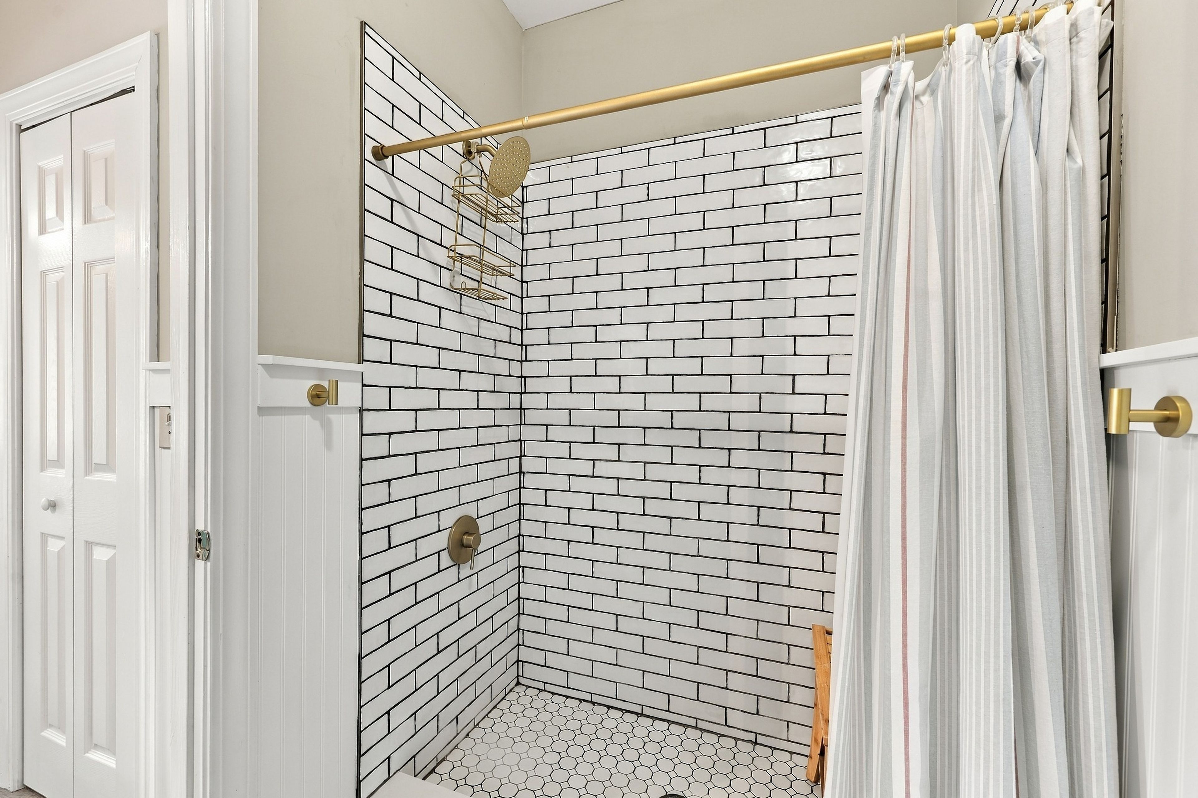 A shower with a white brick wall, a gold showerhead, and a white shower curtain.