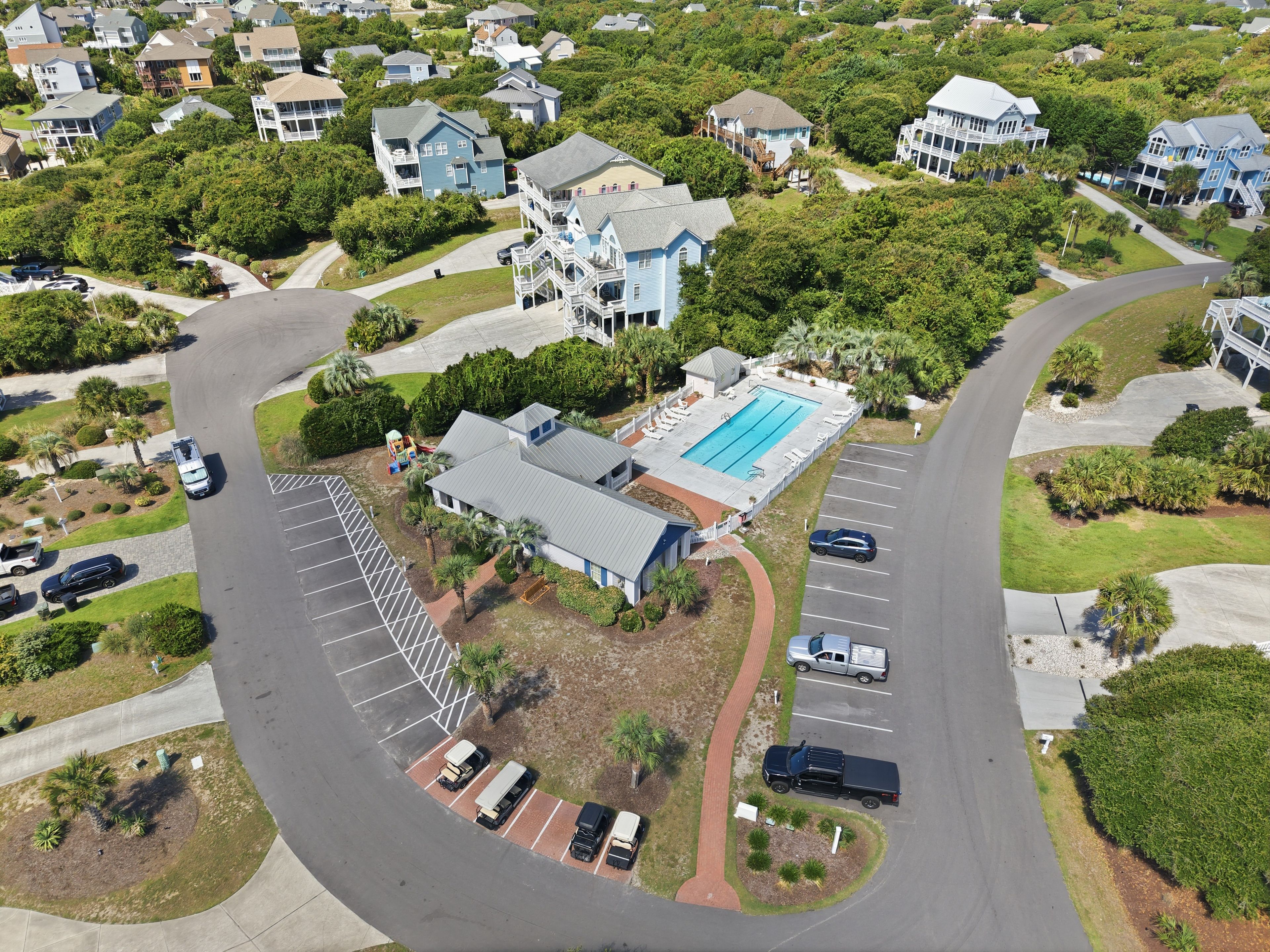 An aerial view of a residential area with a swimming pool, multiple houses, and a parking lot.