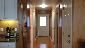 A narrow hallway with wooden walls and a wooden floor, leading to a door with a window. - HONEYHOLE 3BR.  Beautiful, spacious, and best of all...NO BUNK BEDS! (Venice)