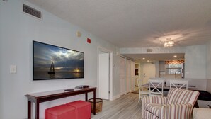 A living room with a large flat-screen TV mounted on the wall, a red bench, a striped armchair, and a small pool table.