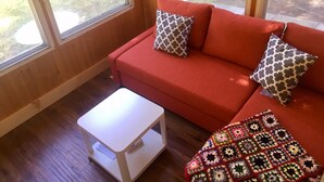 Une pièce chaleureuse avec un canapé rouge, deux coussins à motifs, une petite table blanche et une couverture colorée en crochet.