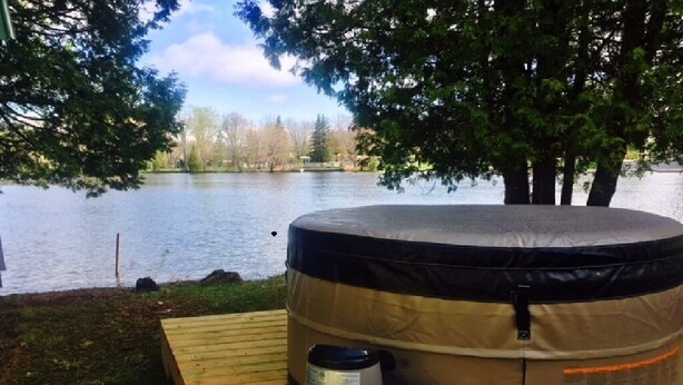 Un bain à remous équipé d’une pompe et d’un panneau de commande, installé sur une terrasse en bois au bord d’un lac.