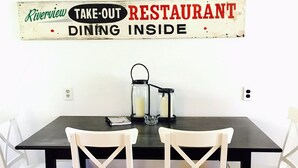 Un espace repas avec une table noire et des chaises blanches, une enseigne au-dessus indiquant qu’il s’agit d’un restaurant proposant des plats à emporter, et un bol bleu accroché au mur.