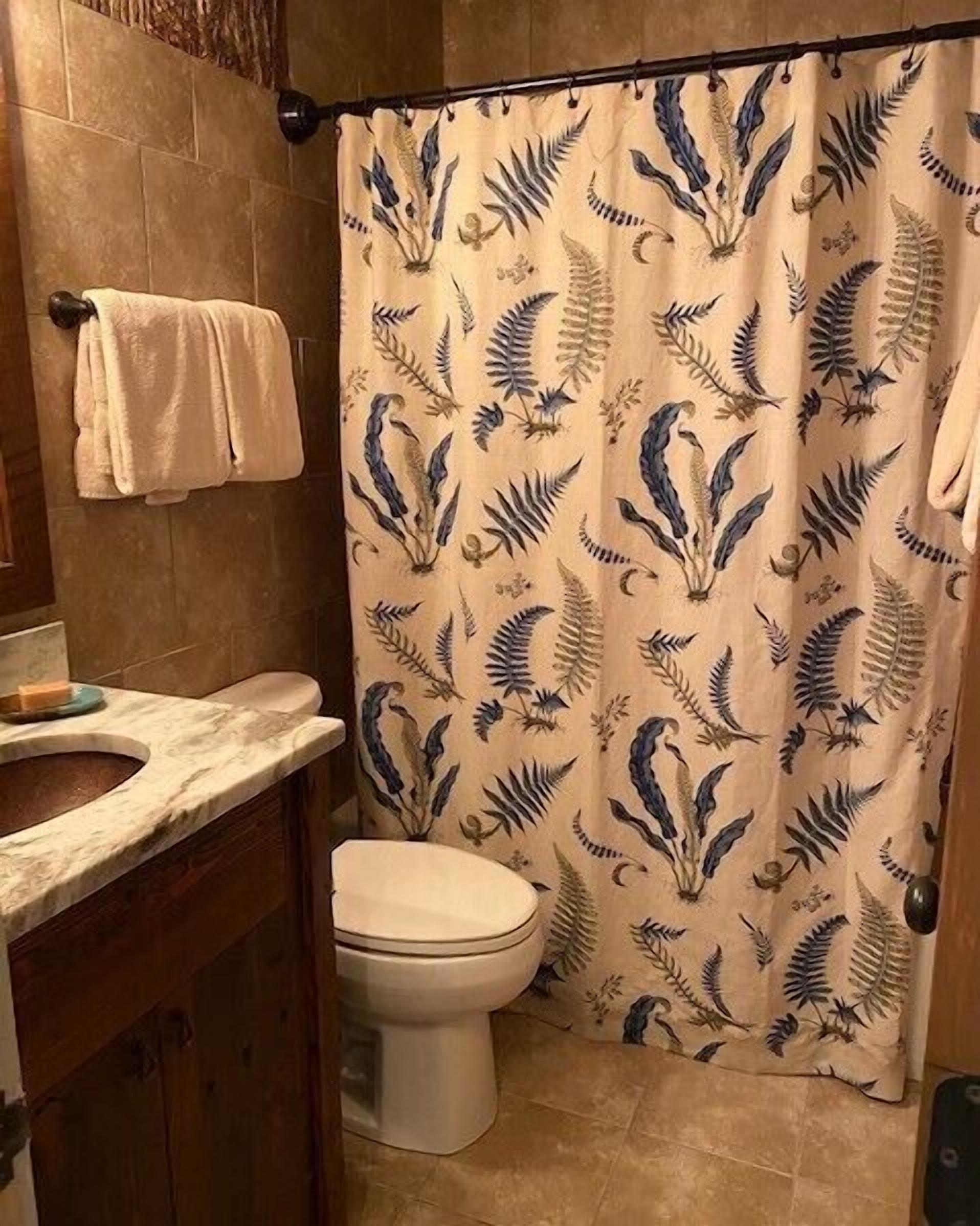 A bathroom with a shower curtain featuring a leaf pattern, a toilet, and a marble sink.