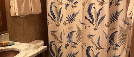 A bathroom with a shower curtain featuring a leaf pattern, a toilet, and a marble sink.
