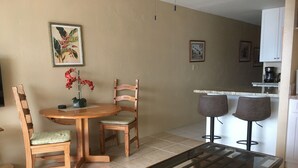 Un comedor con una mesa y sillas de madera, una mesa de centro con cubierta de vidrio y una cocina al fondo.