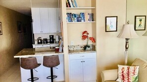 Un espacio habitable compacto con kitchenette, un sofá con cojín floral y una mesa de centro.