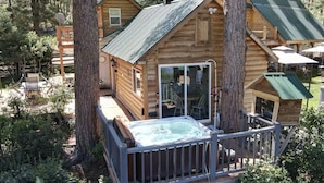 A log cabin with a hot tub, a deck, and a covered patio area.