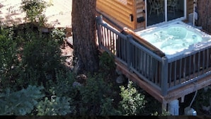 A cabin with a hot tub on a deck, surrounded by trees.