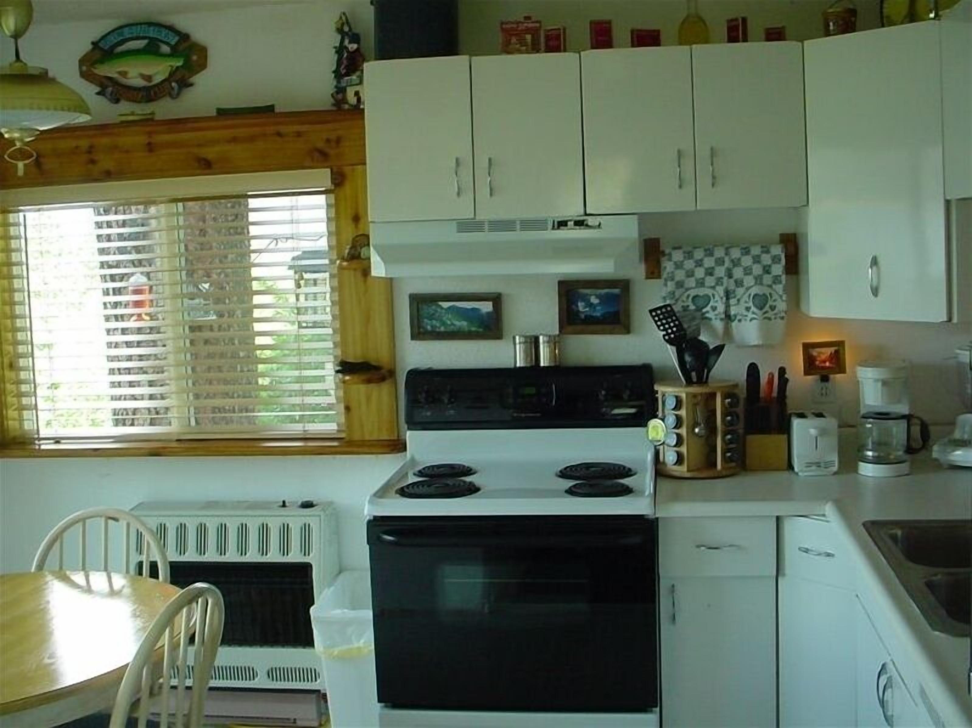 Una cocina con armarios blancos, estufa, microondas y una mesa de comedor con sillas.