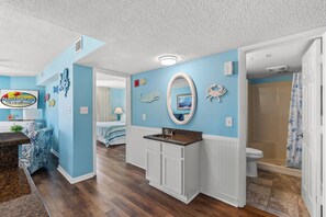 Ein Zimmer mit blauer Wand, Holzboden, Bad mit Duschvorhang und einem Bett mit gestreifter Decke.