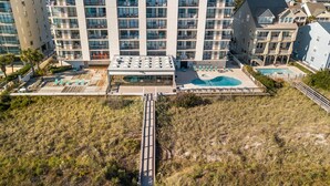 A high-rise hotel with multiple balconies, a rooftop pool, and a boardwalk leading to a beach area.