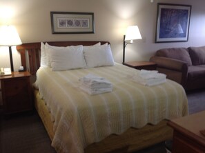 A hotel room with a bed, two bedside tables, a nightstand, a couch, and two wall-mounted lamps. - Rimfire Lodge 307 - Deluxe Full Studio with Full Kitchen, Sleeps 4 (Snowshoe)