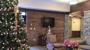 Een gezellige zithoek met een kerstboom, een flatscreen televisie aan een houten wand bevestigd, een stenen openhaard en comfortabele zitplaatsen.