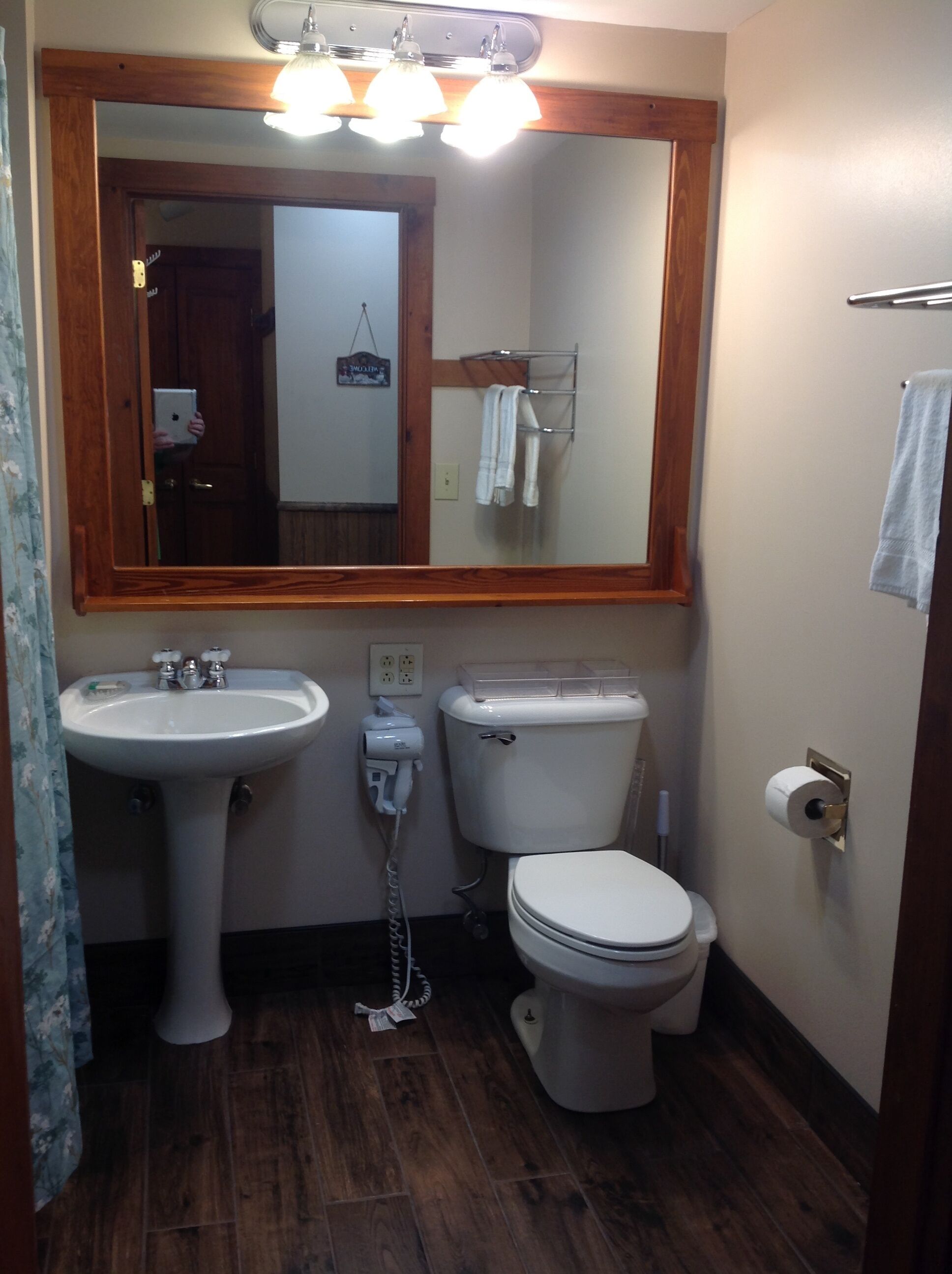 A bathroom with a wooden-framed mirror, a white sink, a toilet, and a towel rack.