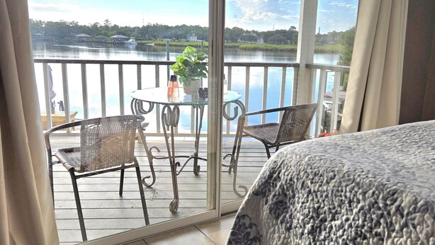 A balcony with a table and chairs, a potted plant, and a view of a lake with boats.