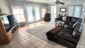 A living room with a television, a leather sofa, a glass coffee table, and a ceiling fan.