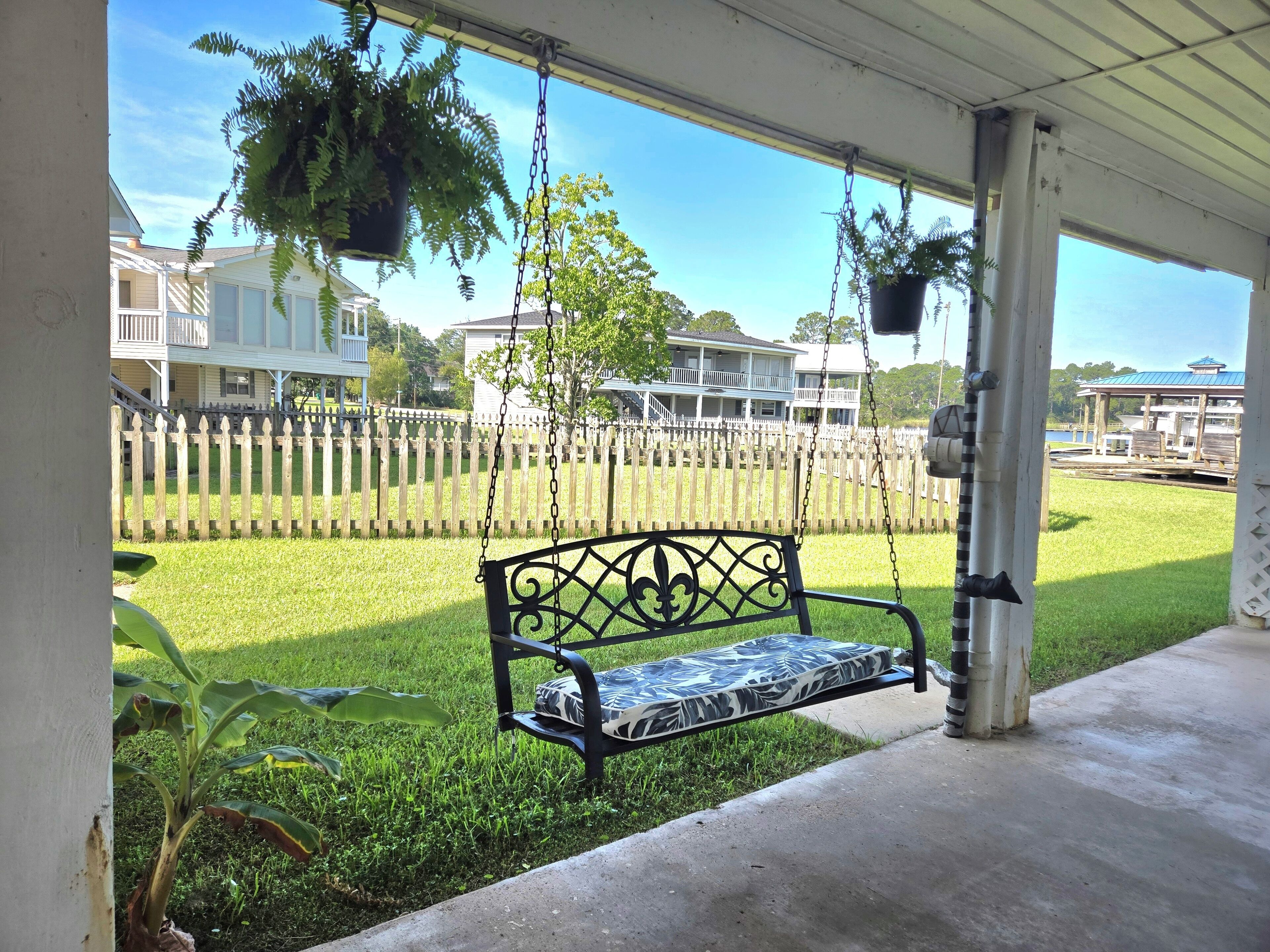 Eine Veranda mit einer Schaukelbank, einem weißen Zierzaun und hängenden Pflanzgefäßen.