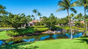 A well-maintained garden with a pond, palm trees, and a building with a red roof. - 🏖️Upgraded Waikoloa Condo w/ Central A/C & Lanai (Waikoloa)