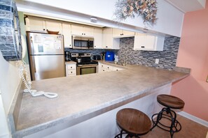 Een keuken met een groot eiland, roestvrijstalen apparatuur en een blauwe tas op het aanrecht.
